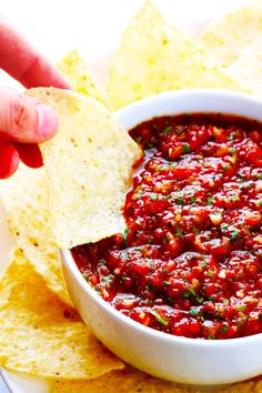 a person dipping salsa into a bowl with tortilla chips on the side,