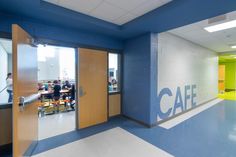 an empty hallway with blue and yellow walls, people sitting at tables in the background