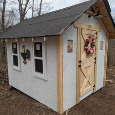 a small white shed with flowers on the door and window sill in front of it