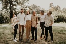 a group of people standing next to each other in a field with trees behind them