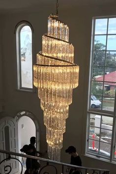 two people are walking up the stairs in front of a chandelier that is hanging from the ceiling