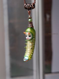 a glass bead necklace with a green caterpillar hanging from it's side