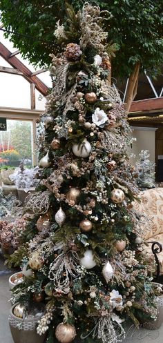 a christmas tree is decorated with ornaments and greenery in gold, silver and white