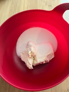 a red bowl with some kind of food in it on top of a wooden table