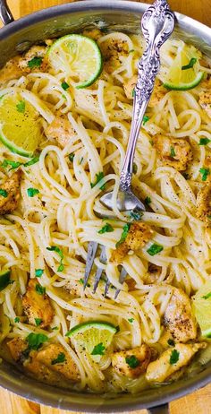 a skillet filled with chicken, noodles and lemons on top of a wooden table