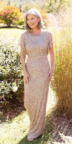 a woman standing in front of some bushes wearing a long dress with sequins on it