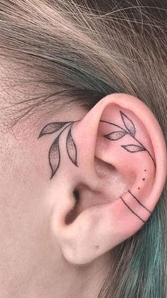 a woman's ear has a small leaf tattoo on it