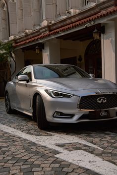 a silver infiniti parked on the side of a road next to a building