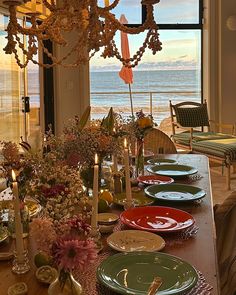 a dining room table with plates and candles on it, overlooking the ocean in front of an open window