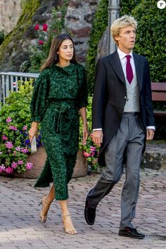 a man and woman are walking down the street in formal attire, one is wearing a suit