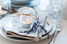 a white plate topped with a glass jar filled with water and lavenders next to a candle