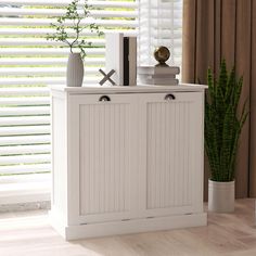 a white cabinet sitting next to a window with blinds on the windowsill and a potted plant