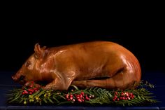 a statue of a cow laying on top of green plants and berries in front of a black background