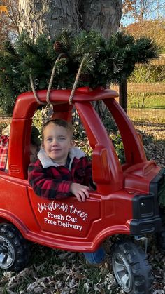 a little boy sitting in a red toy truck with a christmas tree on the top