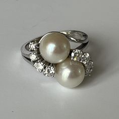 White gold (18k) ring adorned with two beautiful round white Akoya cultured pearls with a very beautiful luster, highlighted with 8 round brilliant-cut diamonds in claw setting. Bead diameter: 9.2 and 9.1 mm. Total weight of diamonds: approximately 0.70 ct. Work from the 1950s/1960s. Gross Weight: 9.70 g. Size: 56 Possibility of sizing, contact us. Further information : We issue an invoice as well as a certificate of authenticity established by our qualified gemologist (LFG Paris). Our photos ar Formal White Diamond Ring With Pearl Drop, Formal White Pear-shaped Diamond Ring, White Diamond Ring With Pearl Drop For Anniversary, Classic White Pear-shaped Diamond Ring, Anniversary Round Diamond Ring With Pearl Drop, Pearl Diamond Ring, Pearl And Diamond Ring, Claw Setting, Pearl Diamond