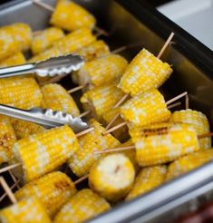 corn on the cob with toothpicks and tongs in a metal container