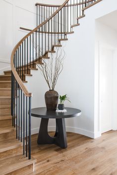 a table with a vase on it in front of a spiral stair case and wooden floors