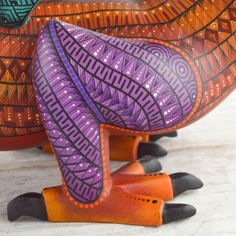 an orange and purple bird statue sitting on top of a white floor next to a wall