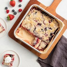 a pan filled with dessert next to plates of strawberries and blueberries on a table