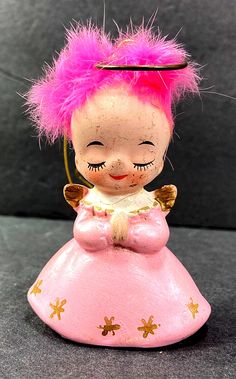 a pink and gold figurine sitting on top of a black table next to a gray wall