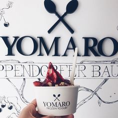 a person holding up a bowl of yogurt with spoons on the side