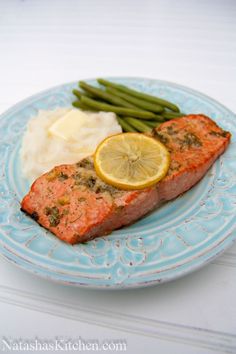 a blue plate topped with salmon, mashed potatoes and green beans next to a lemon wedge