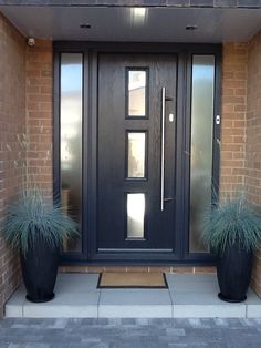 two large black planters sitting in front of a door with glass panels on it