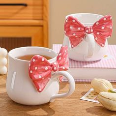 two coffee mugs with pink and white polka dot bows are sitting on a table