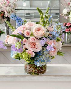 a vase filled with pink and blue flowers on top of a white table next to mirrors