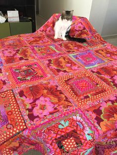 a cat sitting on top of a bed covered in pink and orange quilts,