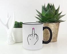 a white and black coffee mug with a pink finger on it next to a succulent plant