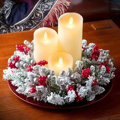 three lit candles sit in a wreath on a table