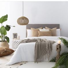 a bed with white linens, pillows and plants