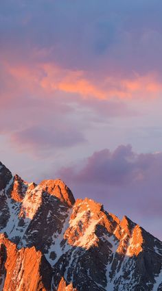 the mountains are covered in snow and pink clouds at sunset or sunrise, as seen from below