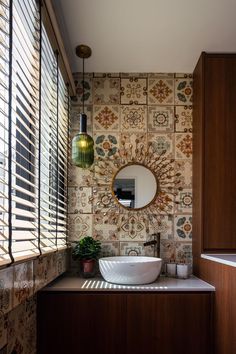 a bathroom sink sitting under a round mirror next to a window with blinds on it