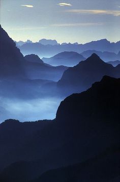 the mountains are covered in fog and low lying clouds at dusk or dawn, as seen from an airplane