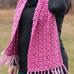 a woman wearing a pink crocheted scarf with tassels on her shoulders