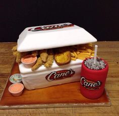 a cake made to look like a cooler with fries and drinks on it, sitting on top of a wooden table