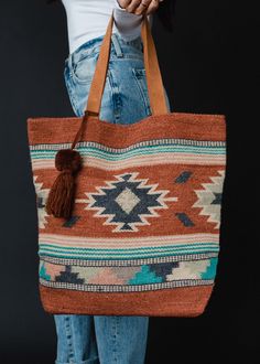 Make a statement on your travels with this eye-catching tote bag! The rust, green and cream Aztec inspired print is a favorite of ours, and we can't wait to bring it along on all our getaways this season. Rust, green, blue and cream Aztec inspired tote bag Rust pom tassel detail Leather suede straps Measures 17" x 6.5" x 14.5" Designed in the U.S.A. Produced in India. 100% Cotton Lining: 100% Polyester Bohemian Canvas Bag With Large Capacity For Travel, Bohemian Canvas Travel Bag With Large Capacity, Bohemian Large Capacity Canvas Bag For Travel, Bohemian Multicolor Bags For Weekend Trips, Bohemian Brown Bags For Weekend Trips, Bohemian Beach Bag With Leather Handles For Travel, Bohemian Brown Weekender Bag For Weekend Trips, Bohemian Brown Canvas Bag With Large Capacity, Brown Rectangular Canvas Bag For Weekend Trips