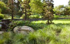 a stone bench sitting in the middle of a lush green field with tall grass and trees