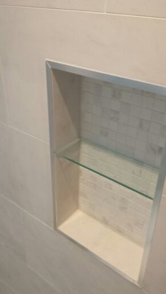 a white bathroom with a glass shelf above the toilet seat and tile on the wall