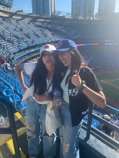 two girls standing in the bleachers at a baseball game with their thumbs up