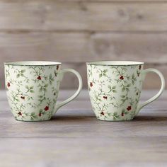 two coffee cups sitting on top of a wooden table next to each other with red flowers painted on them