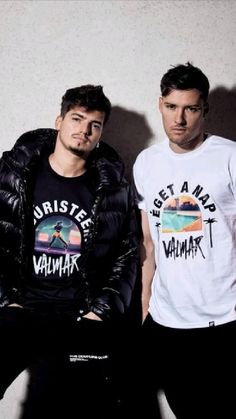 two young men sitting next to each other in front of a white wall wearing t - shirts