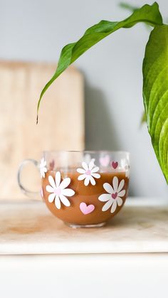 a tea cup with flowers painted on it and a green plant in the back ground