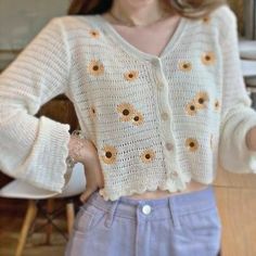 a woman standing in front of a wooden table wearing a white sweater with sunflowers on it