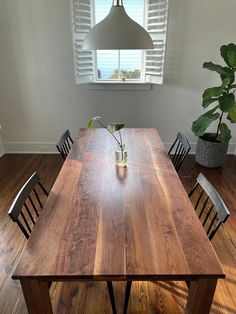 a wooden table with chairs around it and a potted plant in the corner on the other side