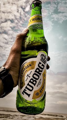 a person holding up a beer bottle in front of a cloudy sky with the word tupperroc on it