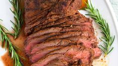 a piece of meat on a white plate with oranges and rosemary garnish