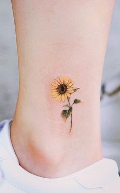 a small sunflower tattoo on the side of a woman's ankle is shown